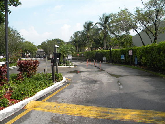 A gated entrance with a road leading into a residential area surrounded by trees and hedges.