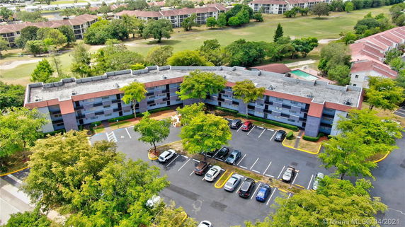 Aerial view of a multi-story residential building with a parking lot and surrounding greenery.