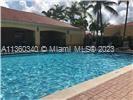 Outdoor swimming pool with adjacent building and palm trees.