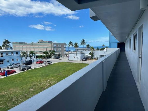View from a building corridor overlooking a grassy area and nearby structures with the ocean in the background.