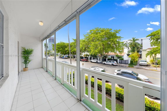 View from a covered balcony overlooking a street with parked cars and trees.