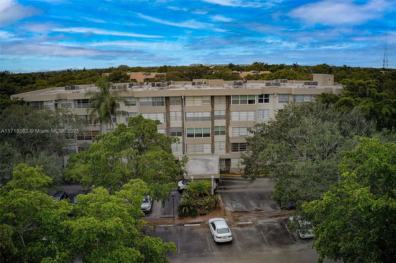 Front view of a multi-story building with parking area and trees in the foreground.