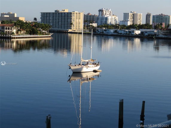View of a calm water body with a docked sailboat and distant buildings on the waterfront.
