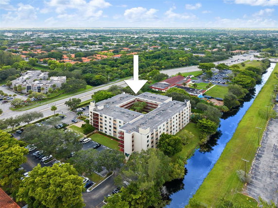 Aerial view of a multi-story apartment building with a flat rooftop and surrounding parking area.