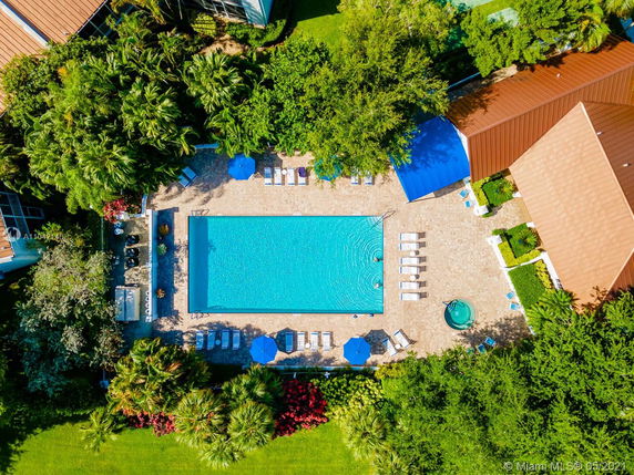 Aerial view of a rooftop area featuring a large swimming pool, lounge chairs, umbrellas, and surrounding greenery.