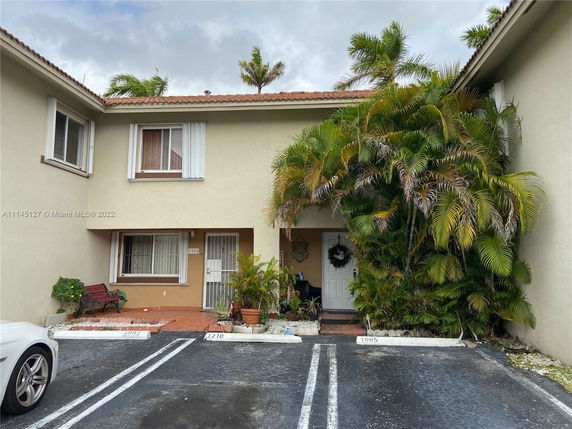 Front view of a two-story house with a tiled roof and palm plants near the entrance.