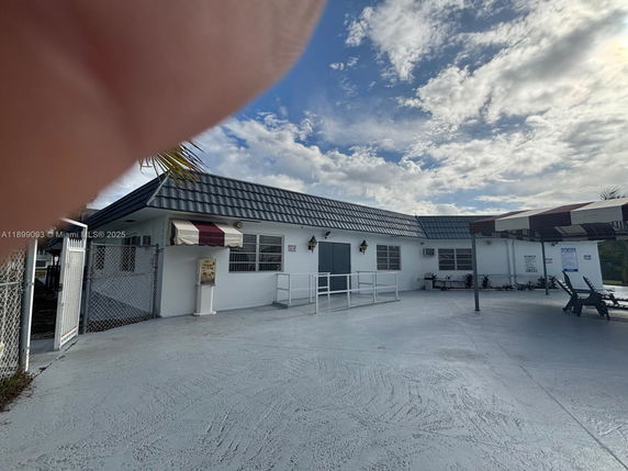 Front view of a single-story building with a metal roof and a covered entrance area with chairs.