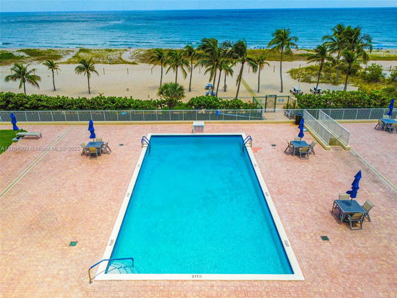 Outdoor swimming pool area with deck chairs and umbrellas near the beach.