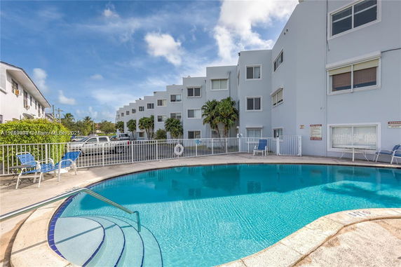 Outdoor swimming pool area adjacent to a multi-story residential building.