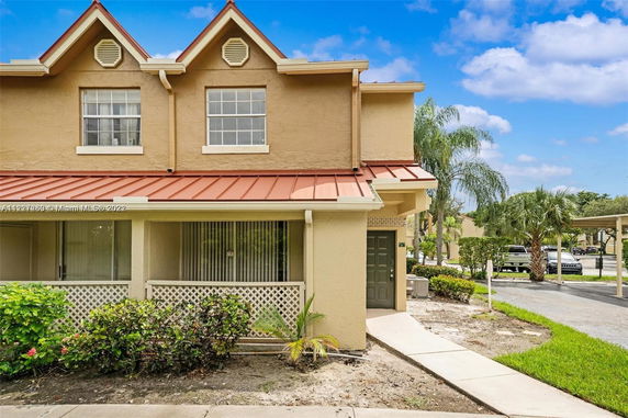 Front view of a two-story house with a red metal roof and lattice porch railing.