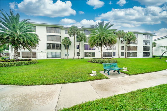 Front view of a multi-story residential building with large windows and a green lawn.