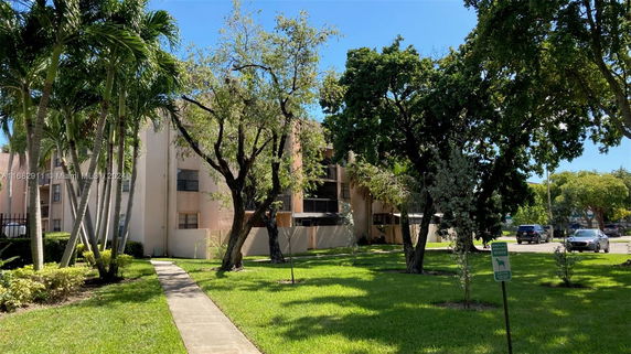 Front view of a multi-story apartment building surrounded by trees and grass.