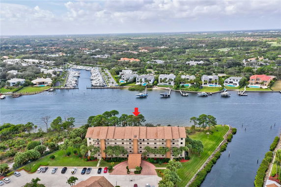 Aerial view of a waterfront building with a marina and residential area across the water.