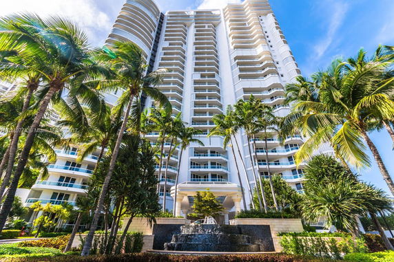 Front view of a tall residential building with multiple balconies and palm trees in front.