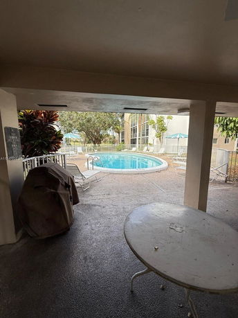 View of an outdoor swimming pool surrounded by a fence, with loungers and a building nearby.