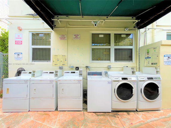 Outdoor laundry area with washing machines and dryers under a canopy.