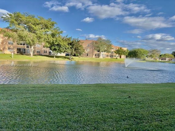 Buildings seen across a pond with a fountain, surrounded by trees and grass.