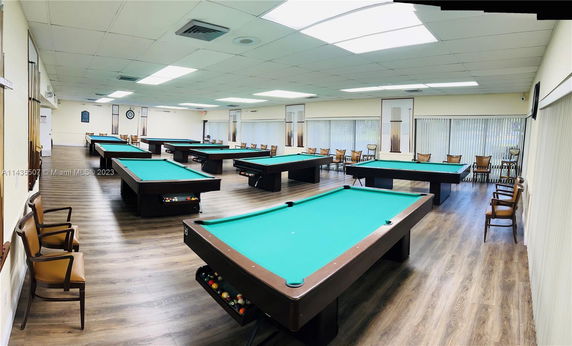 Room with multiple billiard tables and chairs around.