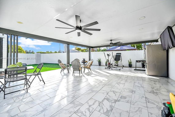 Covered outdoor patio area with ceiling fans, exercise equipment, chairs, and a table.