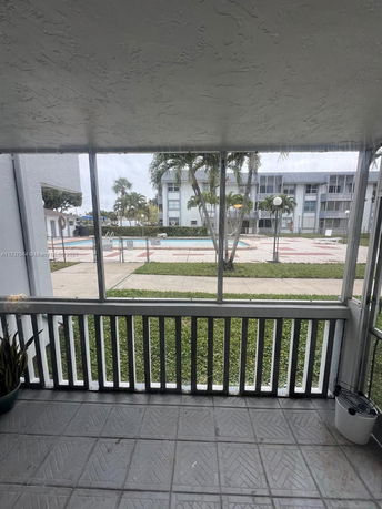View of a swimming pool area with surrounding buildings seen from a partially enclosed patio.