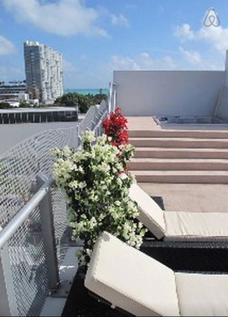 Rooftop area with lounge chairs and plants, overlooking buildings and the ocean.