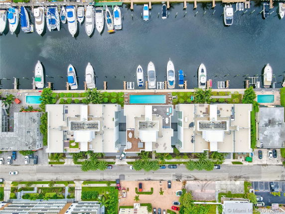Aerial view of modern buildings with flat rooftops, featuring multiple air conditioning units, next to a marina with docked boats.
