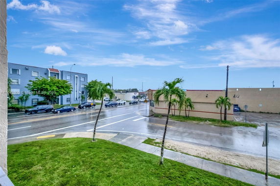View of a street with palm trees and parked cars, adjacent buildings visible.