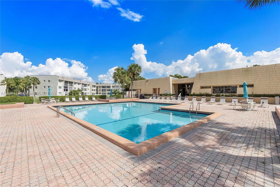 Outdoor swimming pool area with surrounding seating and a building in the background.