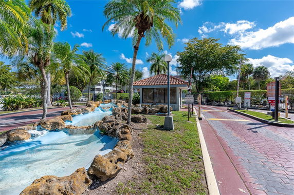 Entrance area with a small building and decorative water feature surrounded by palm trees.
