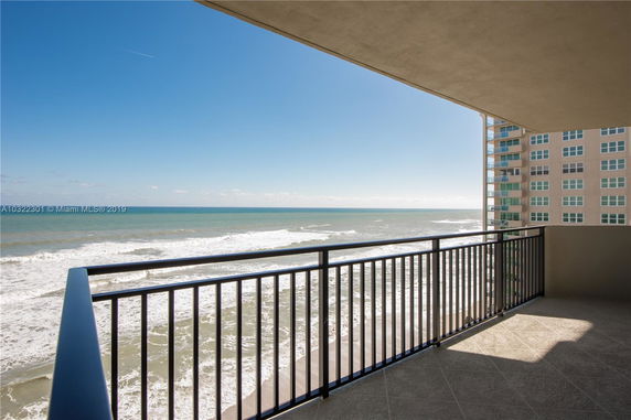 View from a balcony overlooking the ocean with a high-rise building nearby.