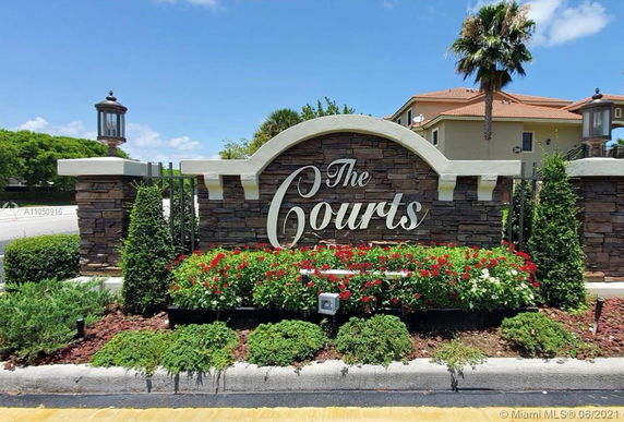 Entrance sign for 'The Courts' with stone wall and surrounding plants.