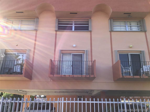 Front view of a multi-story building with balconies and a parking area underneath.