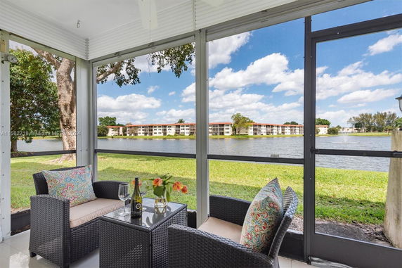 View of a lake and residential buildings from a screened porch area with chairs and a table.