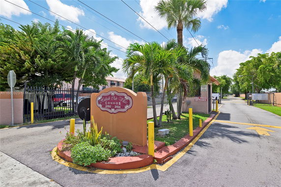 Entrance of a condominium complex with a sign and tropical landscaping.
