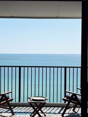 View of the ocean from a balcony with chairs and a small table.