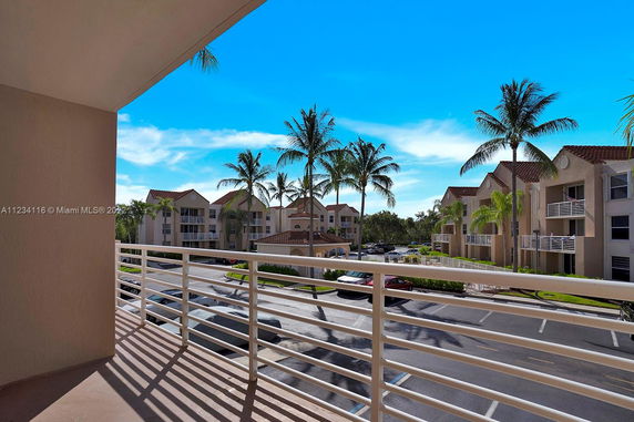 View from a balcony overlooking a residential area with multiple apartment buildings and palm trees.
