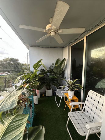 Small outdoor balcony with chairs, plants, and a ceiling fan.