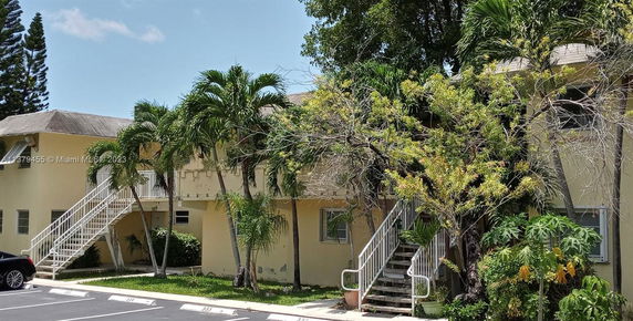Front view of a two-story building with exterior stairs and surrounding greenery.