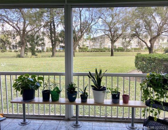 View from a porch with a bench of potted plants overlooking a grassy area and trees.