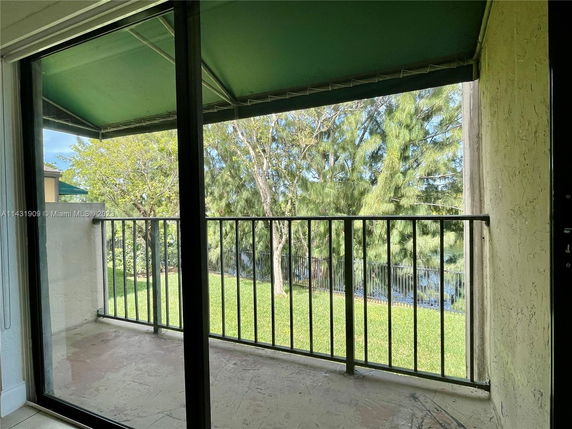 View from a covered balcony with a metal railing and greenery in the background.