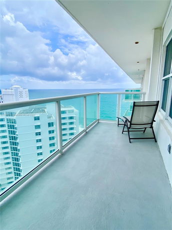 Balcony view overlooking the ocean with a single chair and glass railing.
