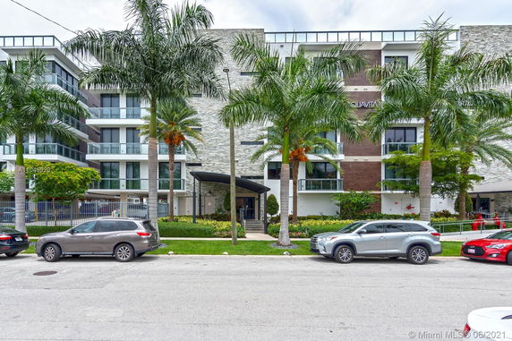 Front view of a multi-story residential building with balconies and palm trees.