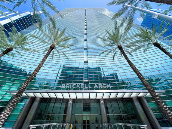 Front view of a high-rise building with glass facade and palm trees at the entrance.