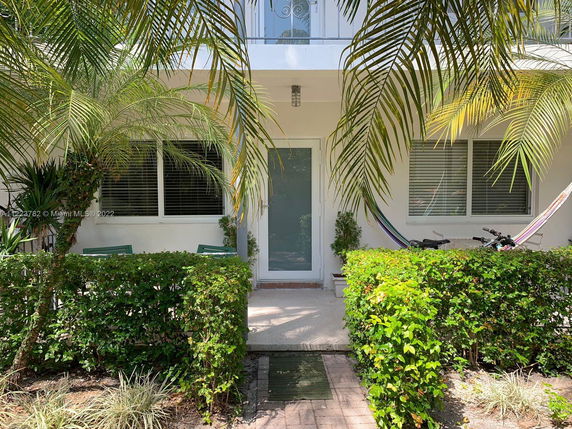 Front view of a house with a glass door and windows, surrounded by plants and trees.
