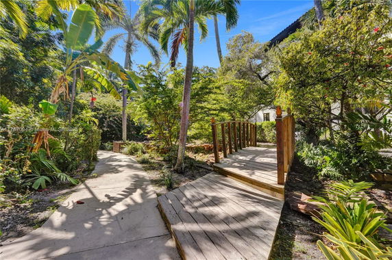 Pathway with wooden bridge surrounded by lush greenery and tall palm trees.
