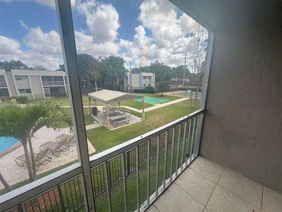 View from a balcony overlooking a communal outdoor area with a swimming pool, lounging chairs, and a covered seating area.