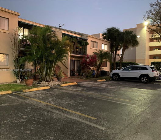 Outdoor view of a two-story apartment building with a parking area in the foreground.