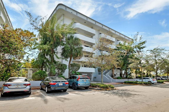 Front view of a multi-story residential building with balconies and surrounding greenery.