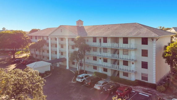 Front view of a multi-story residential building with balconies and a parking area in front.