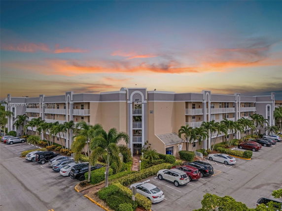Front view of a three-story apartment building with balconies and adjacent parking area.